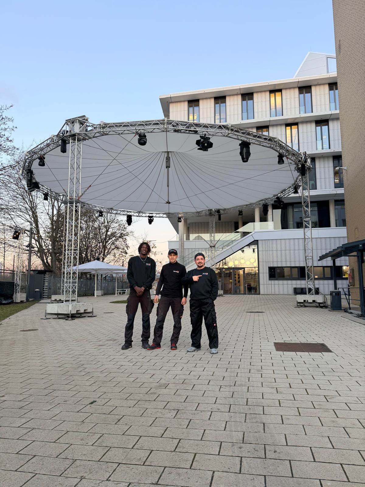 Drei Männer stehen vor einer Veranstaltungsbühne – Servix